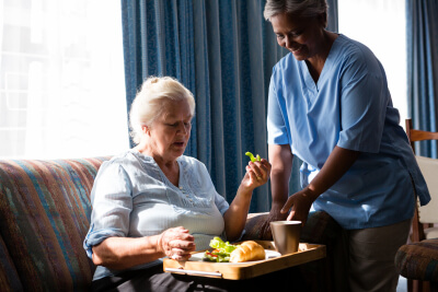caregiver standing by senior woman eating healthy food