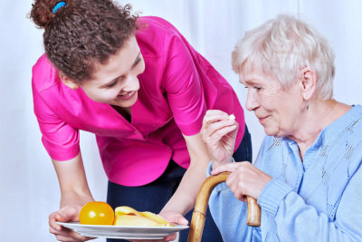 elder woman eating while being assisted by her caregiver