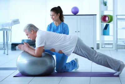 Man exercising with therapeutic ball assisted by his caregiver